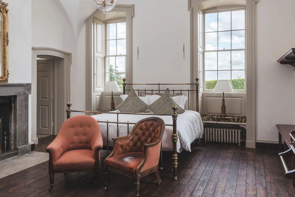 A wing bedroom with a brass bed, leather armchairs and an open fireplace