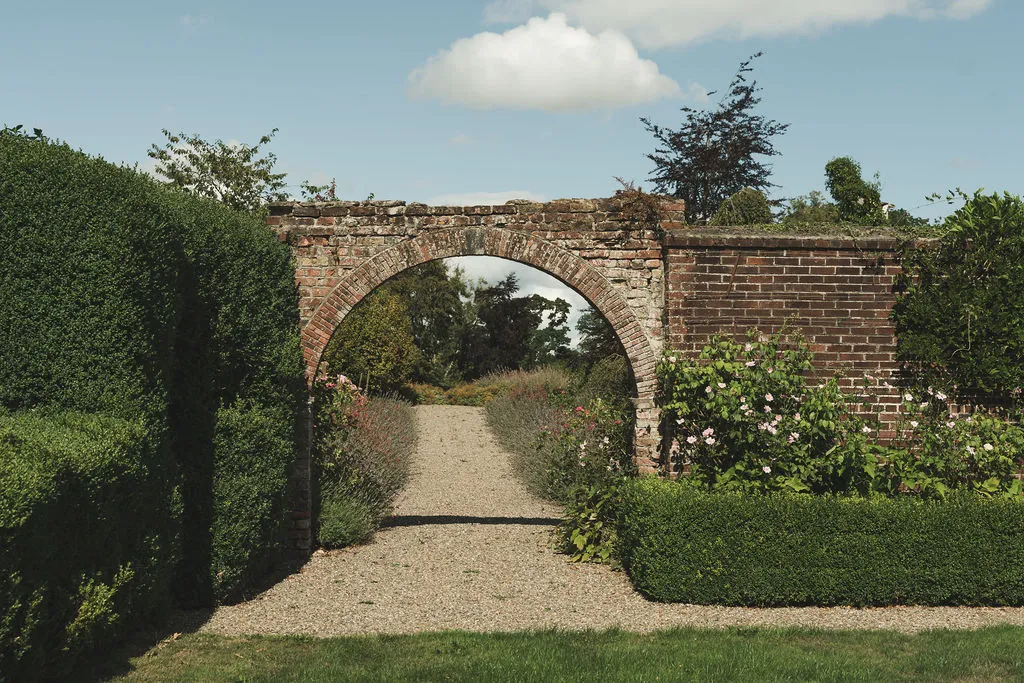 An arched opening in the walled garden, planting soft either side of the path