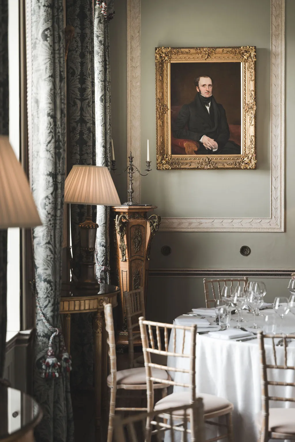 The dining room of the Manor House set for dinner beneath portraits and lamplight