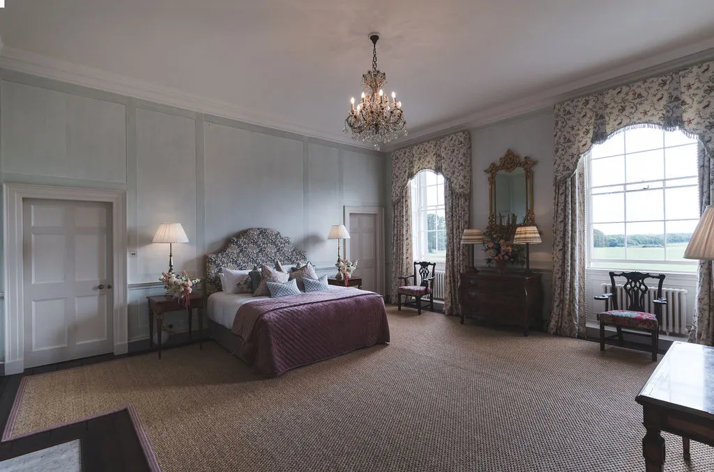 A suite in the Manor House, a chandelier above the bed and tall windows onto parkland